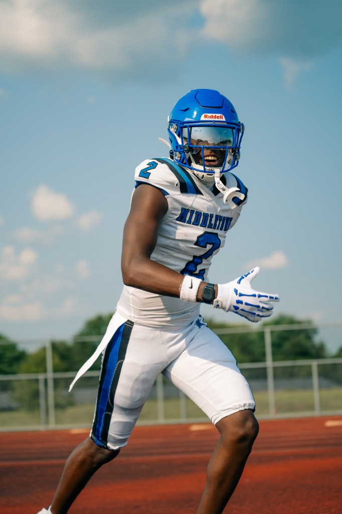 BJ Garrett smiling while running on a track in a white Middletown jersey and blue helmet