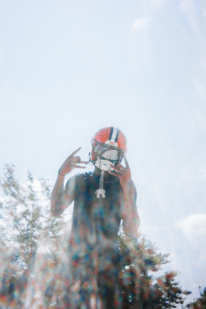 BJ Garrett in a Syracuse orange helmet making hand gestures against a bright sky